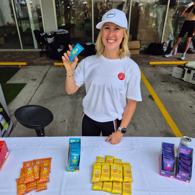 Person holding a product at an outdoor event with various items on a table.